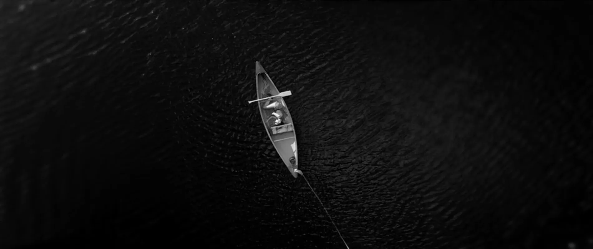 Afterlife still: a canoe on dark water, seen from above